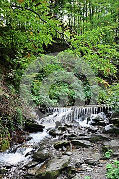 Close-up image of a small wild waterfall in the form of short streams of water between mountain stones