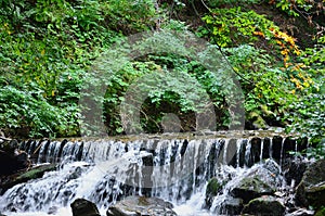 Close-up image of a small wild waterfall in the form of short streams of water between mountain stones