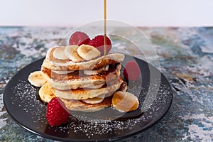 Close-up image of a stack of fluffy pancakes with fruit and maple syrup