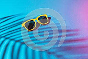 Close-up image of sunglasses on turquoise blue background with palm tree shadow