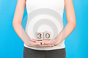 Close up image of thirty weeks of pregnancy cubes in pregnant woman`s hands at blue background. Happy pregnancy. Copy space
