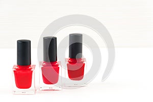 Close-up image of three Red nail polish bottles on white wooden background