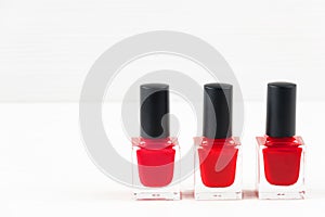 Close-up image of three Red nail polish bottles on white wooden background