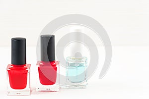 Close-up image of three Red nail polish bottles on white wooden background