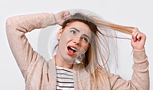 Close up image of upset young woman trying comb unruly hair pulling strands with raised hands screaming from pain and discomfort,