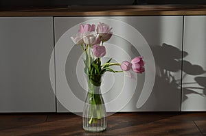 Close-up image of a vase filled with vibrant pink tulips arranged against a white countertop