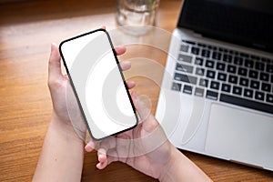 Close-up image of a white-screen smartphone in a woman's hands above a wooden desk with a laptop