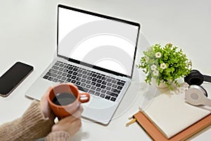 Close-up image of a woman in cozy sweater holding a coffee mug at her desk. laptop mockup