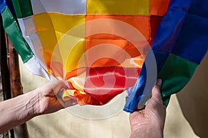 Close-up image of woman\'s hands clutching a silk Wiphala flag, a symbol commonly used to represent the native photo