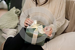 Close-up image of a woman is unwrapping a Christmas gift on a couch in her living room on Christmas