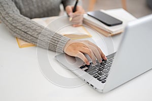 A close-up image of a woman is working on her laptop in a modern office, typing on the keyboard