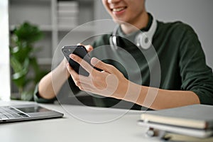 Close-up image of a young Asian man using his smartphone at his desk in his home office