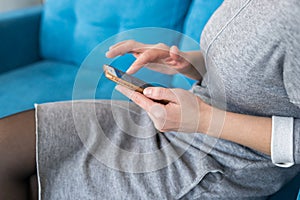 Close-up image of young hipster girl sitting at cozy home interior and using modern smartphone device, female hands typing text me