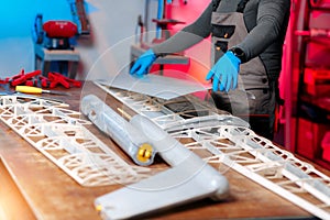 Close-up image of young male engineer or technician working on drone details in lab. Plane wing.