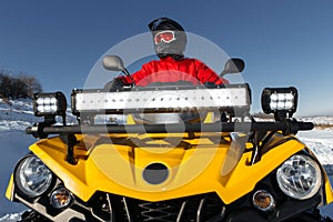 Close-up image of young man driver on the ATV 4wd quad bike stand in heavy snow with deep wheel track.