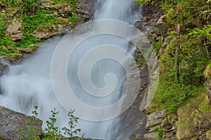 Close-up of an impetuous jump of a waterfall in the midst of mountain vegetation