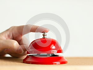 Close-up of index finger pressing the bell button of red vintage style handbell on wooden table