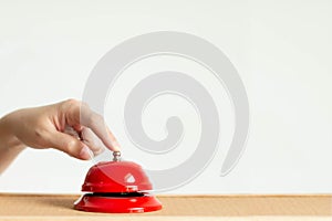 Close-up of index finger pressing the bell button of red vintage style handbell on wooden table