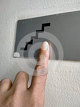 The close up of index finger is pressing the botton stair symbol on the wall in the office room