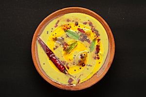 Close-up of Indian traditional kadhi or kadi pakora yogurt and gram flour and turmeric served hot in a clay bowl.