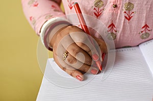 Close up of an Indian woman's hands writing in notepad with pen placed on hand