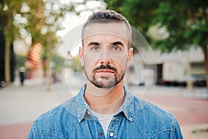 Close up individual portrait of handsome serious guy looking at camera standing outdoors. Front view of young real man