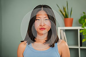 Close up individual portrait of serious asian young woman looking at camera standing at home linving room. One photo