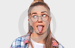 Close up indoors shot of pretty young blonde woman dressed casual outfit and eyewear, making funny faces at camera, sticking out