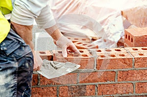 Close up of industrial bricklayer laying bricks on cement mix on construction site