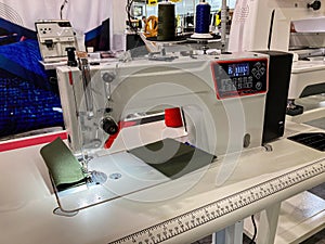 Close-up of an industrial sewing machine in a workshop, against other machinery Needle threaded and digital readouts present