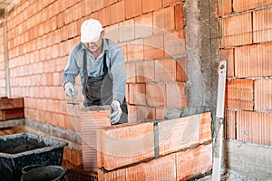 Close up of industrial worker, bricklayer installing bricks on interior building at construction site