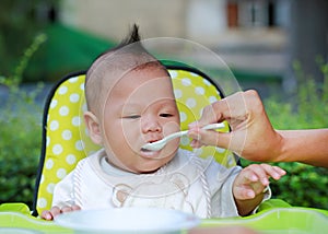 Close up infant baby boy feeding food on the kid chair in the garden. First time infant baby for feeding food