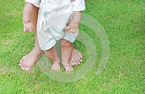 Close up infant baby feet learning to walk with his mother on the green grass. First steps
