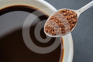 Close up of Instant Coffee on Stainless Steel Tea Spoon with Black Coffee in White Cup, Black Background