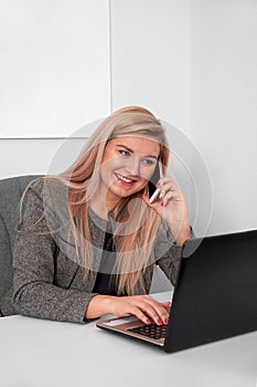 Close up of an interested businesswoman in a suit working at her white office. She is talking on phone and work with