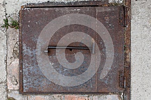 Close-up of the iron cover of a square manhole in the cement floor. Large rusty lid hinges. Entrance to the bunker