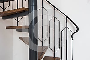 Close up of a iron exterior spiral staircase on the side of a modern house with white wall
