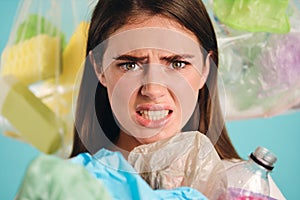 Close up irritated girl with plastic waste around scaredly looking in camera over colorful background isolated