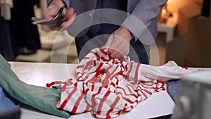 Close-up. An irritated man cuts white clothes with red stripes with scissors and nervously throws them on the table.