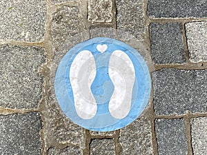 Close up of isolated blue marking sign with feet on the floor to wait here and keep distance while queueing at shop entrance