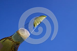 Close up of isolated bottleneck with sparkling yellow beer and a slice of lime against cloudless deep blue sky