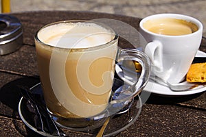 Close up of isolated brown dutch milk coffee koffie verkeerd in transparent glass mug and white espresso cup