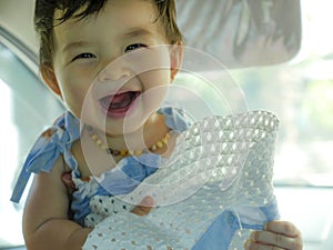 Close up isolated face portrait of sweet and adorable Asian Chinese baby girl laughing and smiling cheerful holding hat enjoying