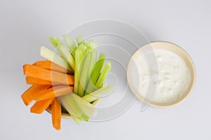Close up isolated flat lay top view shot of party snack food. A bowl of crunchy orange carrot and juicy green celery sticks with a