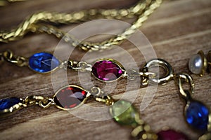 Close up isolated group gold precious jewellery chains and colorful gem bracelet on wood table