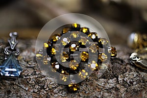 Close up of isolated old vintage brooch with yellow citrine quartz gemstones on natural tree trunk bark background