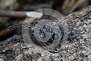 Close up of isolated old vintage silver brooch on natural tree trunk bark background selective focus on brooch left of center