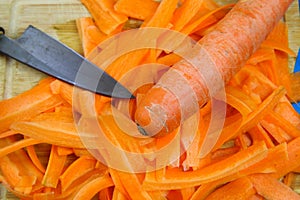 Close up of isolated raw fresh carrot cut in stripes with blade of japanese kitchen knife on wood cutting board