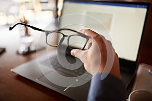 Close-up isolated shot of mans hand holding eyeglasses in front of laptop screen with charts and diagrams. Poor eyesight