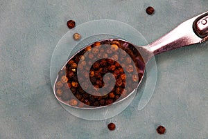 Close up of isolated silver spoon full with red and black cambodian kampot pepper seeds on old blue scratched china dish